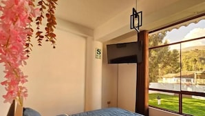 A bedroom with a bed, a TV, and a window with a view of greenery. - Hotel Catañuñi  (Huancayo)