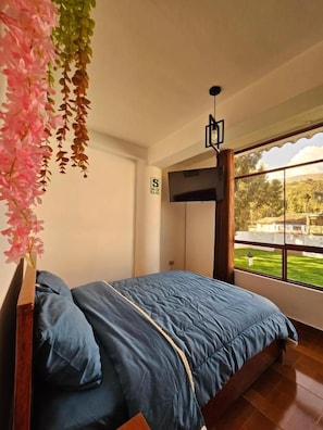 A bedroom with a bed, a TV, and a window with a view of greenery. - Hotel Catañuñi  (Huancayo)
