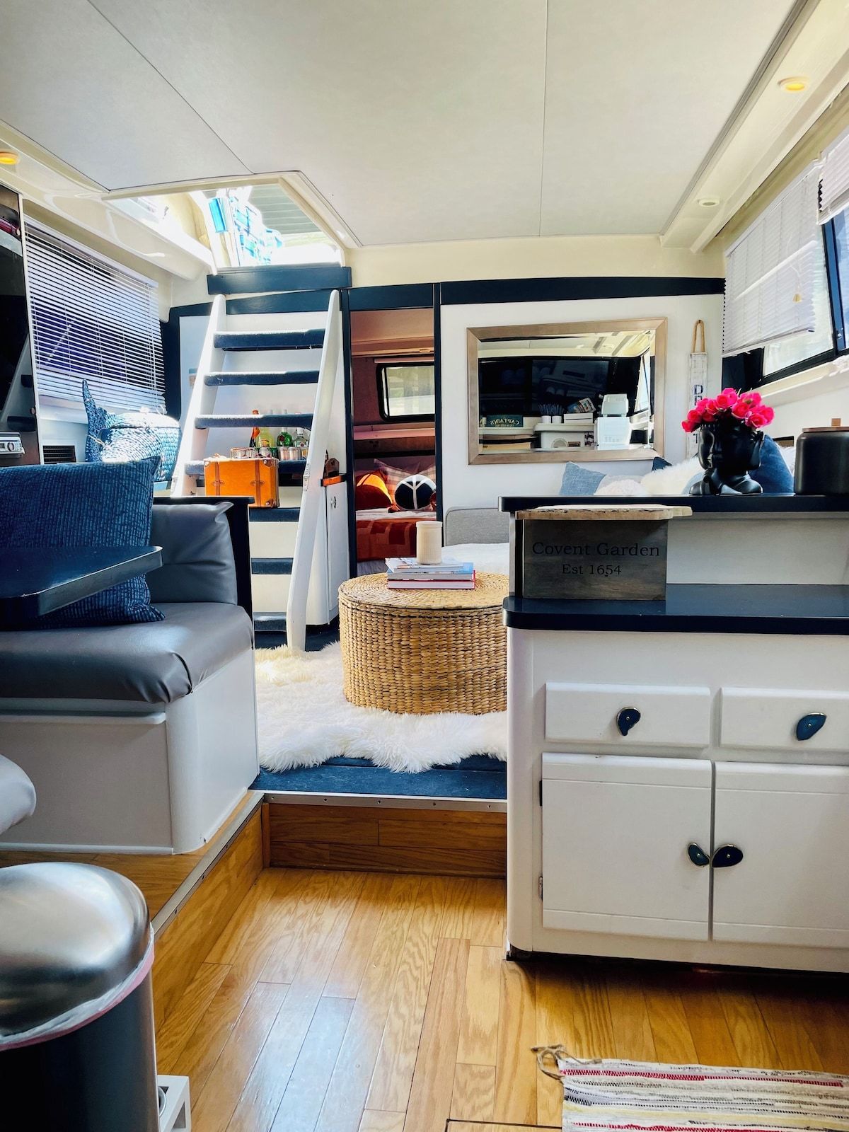 A compact living space with a kitchenette, a sofa, a dining area, and a small staircase leading to an upper level.