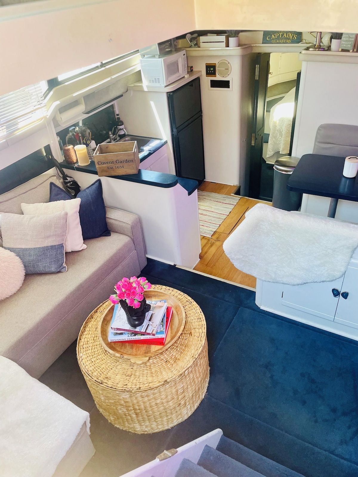 A compact living space with a sofa, a small round table with a book and flowers, a microwave, a television, and a cabinet.