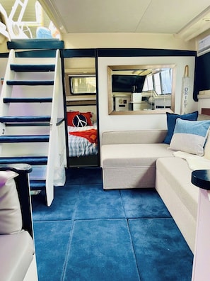 Un espacio habitable compacto con sofá, cama con manta roja y blanca, kitchenette pequeño y escalera.