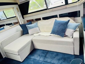A boat interior with a sofa, pillows, and a window.