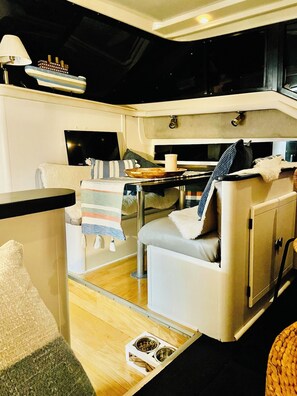 A compact living space with a sofa, a small table, a ship decoration, and a dining area with a bowl and a cup.
