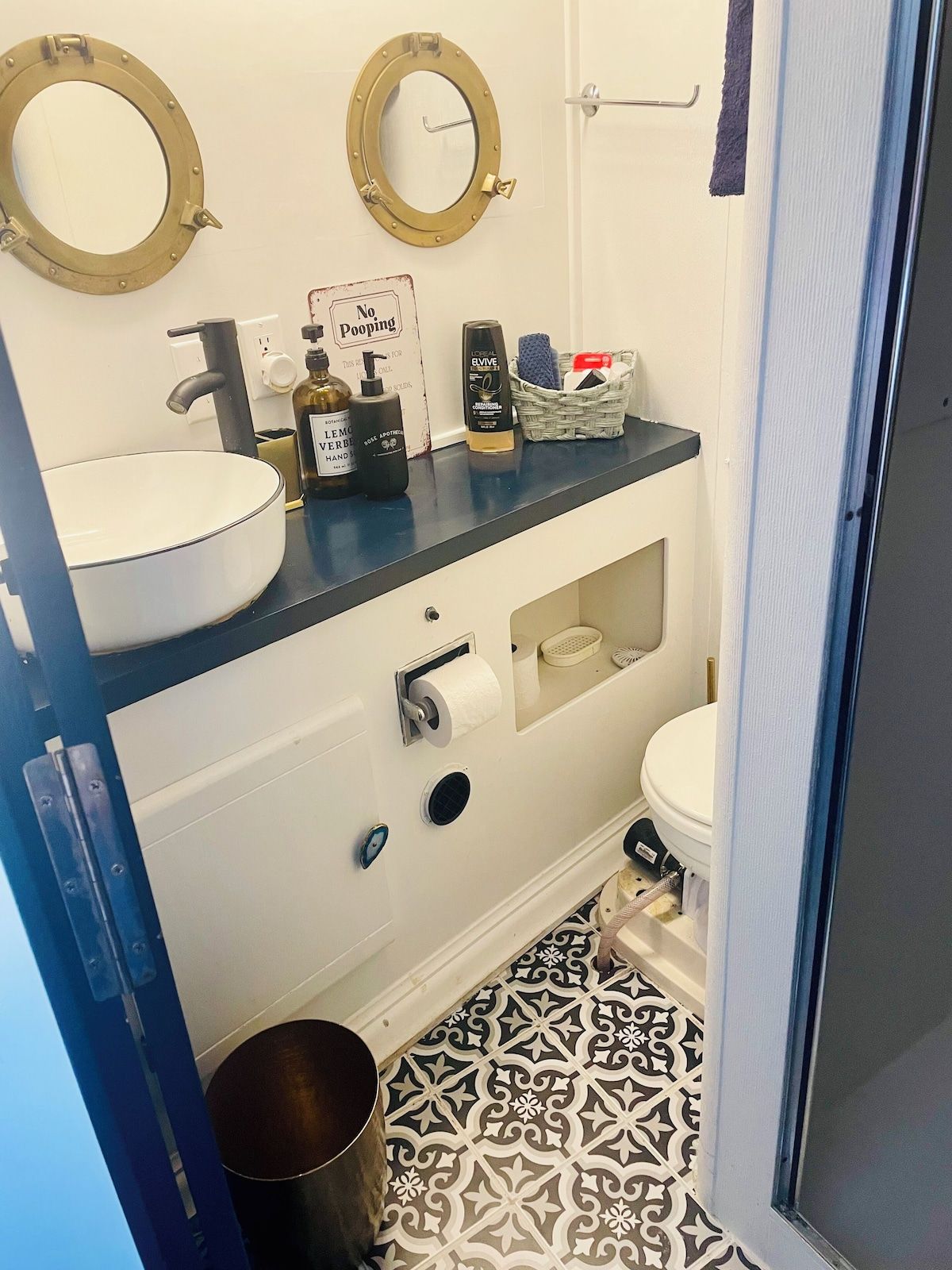 A bathroom with a white sink, a toilet, and a bidet. There are two round mirrors on the wall, a small trash can, and a basket with toiletries.