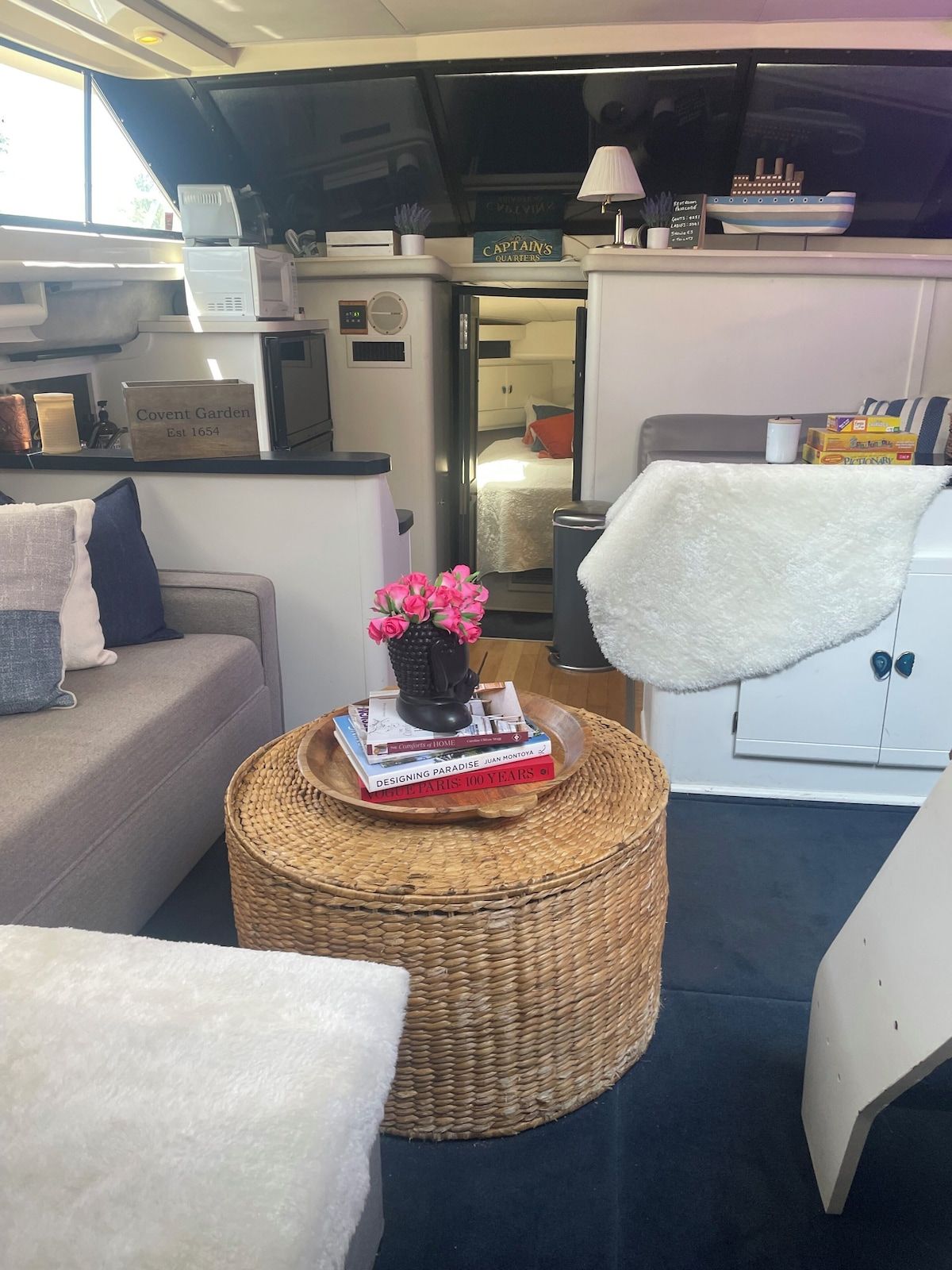 A cozy interior with a sofa, a wicker coffee table with books, a white cabinet, and a sign indicating a garden.