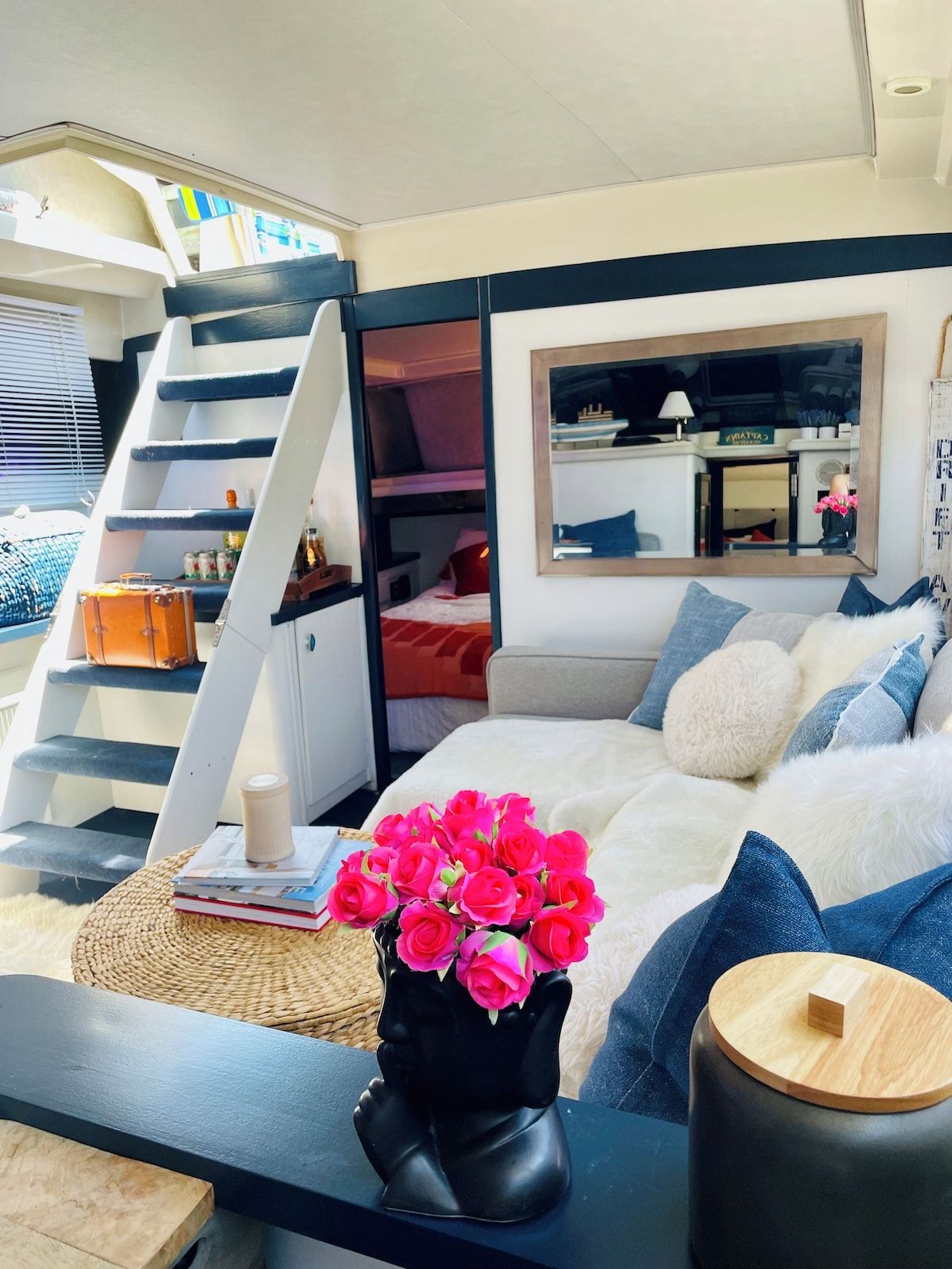 A modern bedroom with a bed, a small table with a vase of flowers, a bookshelf, and a staircase.