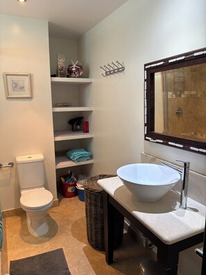 Een badkamer met toilet, wastafel, spiegel, planken met toiletartikelen en een douche.