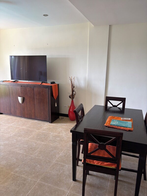 Een eethoek met een donker houten tafel, twee stoelen, een rode vaas en een flatscreen televisie op een standaard.