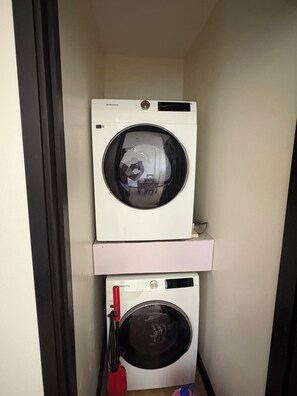 Een wasserette met twee gestapelde wasmachines, een bovenop de ander, en een rode dweil die tegen de muur staat.