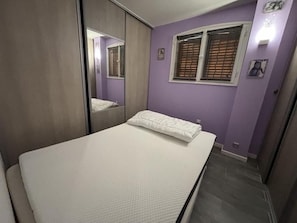 Ein Schlafzimmer mit einem Bett, einem Fenster mit Jalousien, einem Spiegel und einer Wandleuchte.