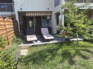 Ein Wohnhaus mit überdachter Terrasse, zwei Liegestühlen, einem kleinen Garten und einem Holzzaun.