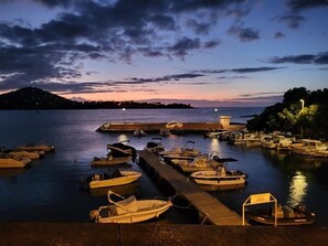 Eine Marina mit an Holzstegen vertäuten Booten, ein Steg, der sich ins Wasser erstreckt, und eine ferne Hügellandschaft.