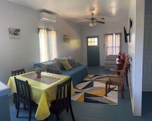 A compact living space with a dining area, a sofa, a ceiling fan, and a door. - 2-bedroom apartment in the heart of Pensacola Roatan with cool ocean breeze (Roatan)