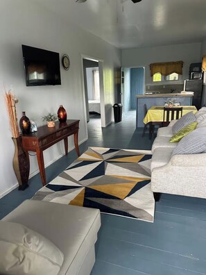 A living room with a sofa, a coffee table, and a TV. There is a hallway leading to a kitchen area. - 2-bedroom apartment in the heart of Pensacola Roatan with cool ocean breeze (Roatan)