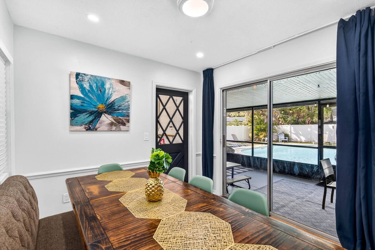A conference room with a wooden table, chairs, a decorative centerpiece, a large abstract painting, and a view of an outdoor swimming pool.