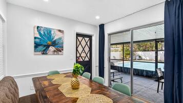 A conference room with a wooden table, chairs, a decorative centerpiece, a large abstract painting, and a view of an outdoor swimming pool.