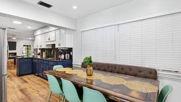 A modern kitchen with white cabinets, a central island, and a dining area with a wooden table and green chairs.