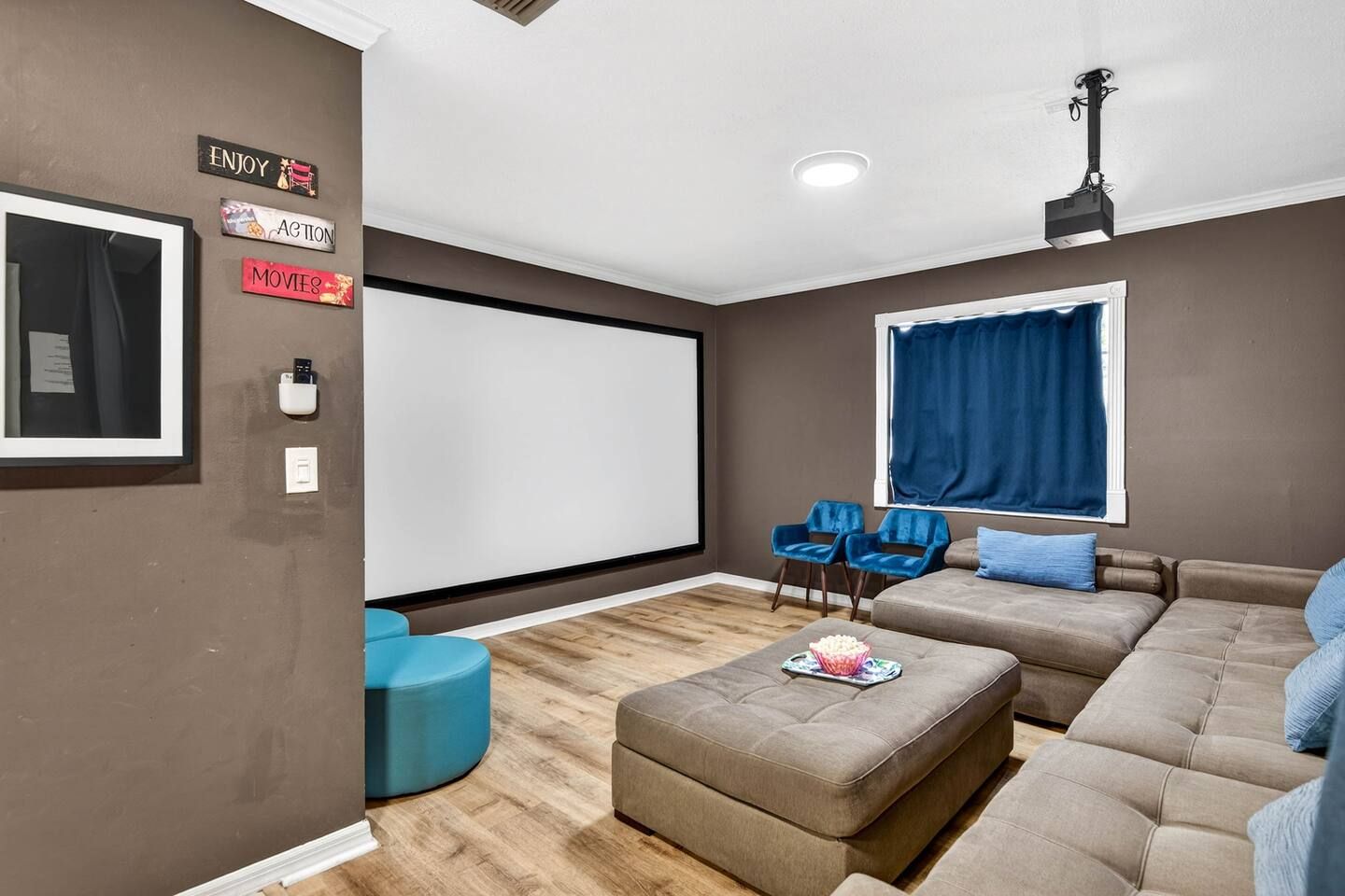 Ein Wohnzimmer mit großem Bildschirm, blauen Sesseln, einer Couch und einem Couchtisch.
