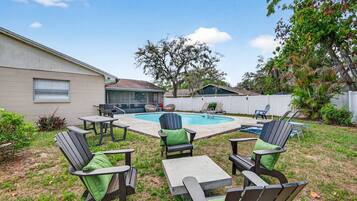 A backyard with a swimming pool, outdoor seating, and a covered patio area.