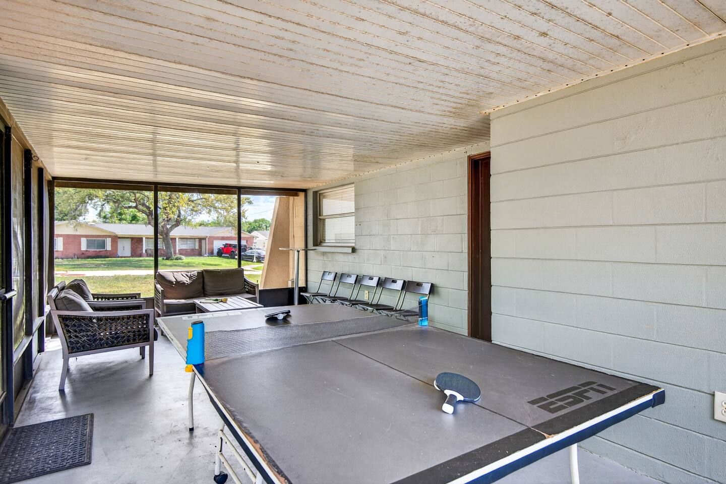 Una mesa de ping pong en una habitación con vistas a una zona residencial a través de amplios ventanales.