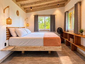 Quarto com cama de madeira, um ventilador, janela com cortinas e prateleira com uma planta.