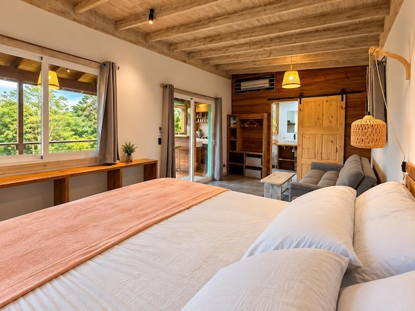 A bedroom with a large bed, a desk, and a view of the outdoors.
