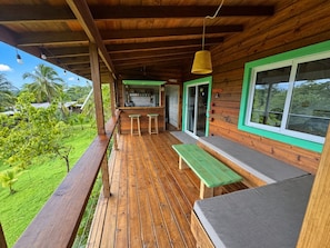 A wooden deck with a bench and a table, overlooking a lush green landscape.