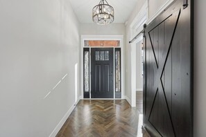 Ein Flur mit Holzboden, einer schwarzen Tür mit Fensterteil und einem Metallgitter.