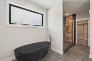 Ein modernes Badezimmer mit einer freistehenden Badewanne, einer Duschkabine aus Glas und Blick durch ein Fenster.