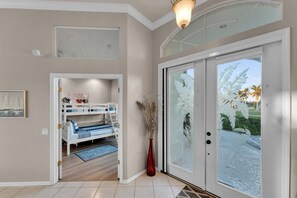 Une chambre avec un lit superposé, un vase contenant des plantes séchées et une vue à travers une porte vitrée.