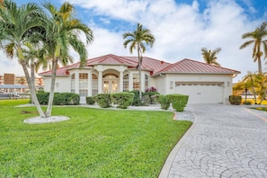 A two-story house with a red roof, a garage, and a well-maintained lawn with palm trees. - Casa Di Sorrento Gulf Access (Cape Coral)