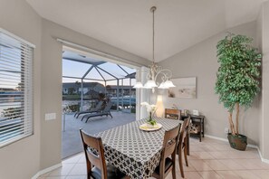 A dining area with a table set for four, a chandelier, and a potted plant. - Casa Di Sorrento Gulf Access (Cape Coral)