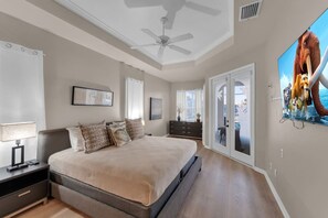 A bedroom with a bed, nightstand, lamp, ceiling fan, and a large window. - Casa Di Sorrento Gulf Access (Cape Coral)