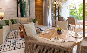 Ein modernes Wohnzimmer mit einer Couch, Sesseln, einem Esstisch für vier Personen und Blick auf Grünflächen.