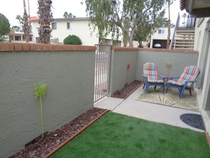 A patio area with a small lawn, two striped chairs, and a wall with a plant.