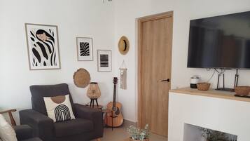 Een moderne woonkamer met een grijze bank, een houten salontafel, een gitaar en een televisie op een dressoir.