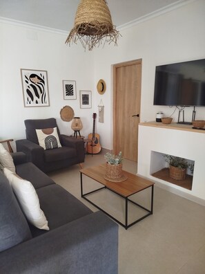 Un salon moderne avec un canapé gris, une table basse en bois, une guitare et un téléviseur posé sur un meuble.