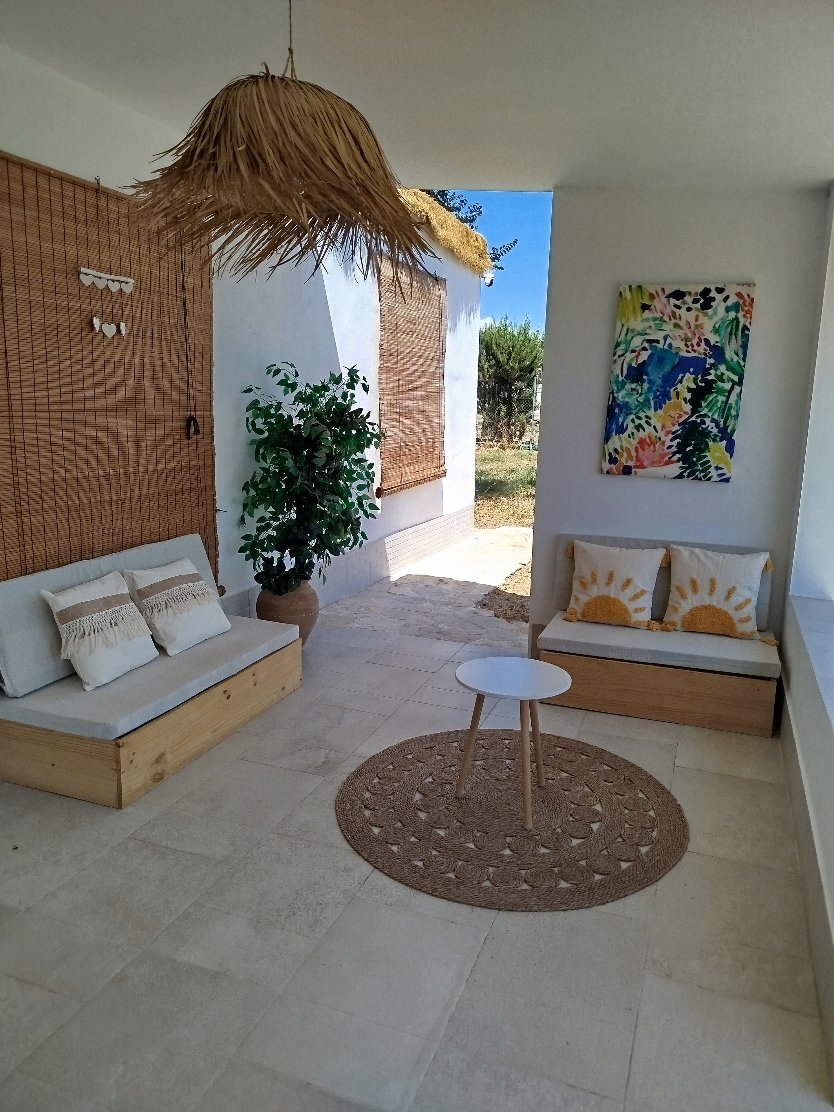 Un área de estar exterior moderna con techo de paja, una planta en maceta y un cuadro abstracto de colores en la pared.