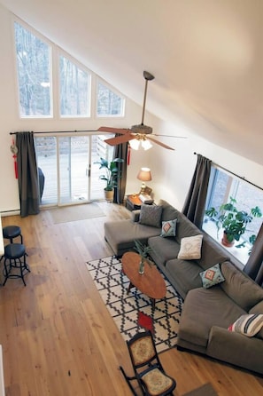 A modern living room with a sofa, a coffee table, and a ceiling fan. There is a sliding glass door leading to a balcony. - Secluded Catskills Retreat w/ Hot Tub & Views (Jewett)