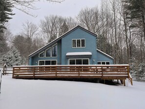 Ein zweistöckiges Haus mit blauer Fassade, einer Veranda und einem Holzzaun in winterlicher Landschaft.
