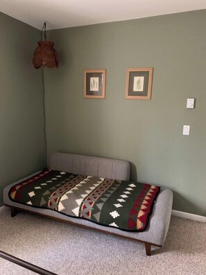 Ein Schlafzimmer mit einem Einzelbett, einer hängenden Deckenleuchte und zwei gerahmten Bildern an der Wand.