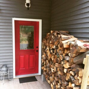 A red door with a glass panel, a stack of firewood, and a metal pot on a stand. - Secluded Catskills Retreat w/ Hot Tub & Views (Jewett)