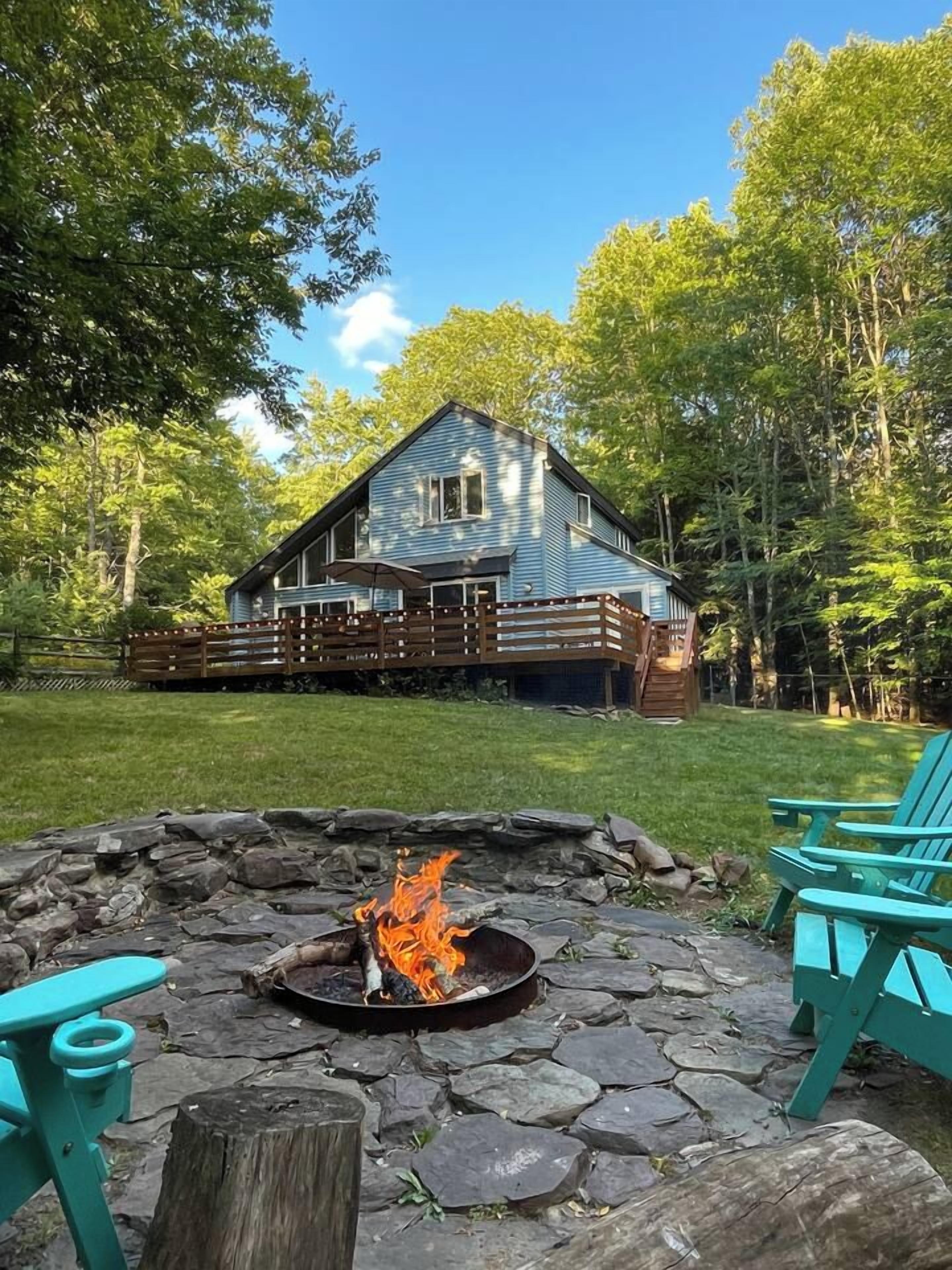 A house with a deck, a stone fire pit, and turquoise chairs.