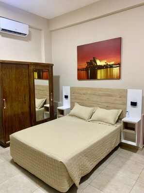 Habitación de hotel con cama, armario, mesita de noche y aire acondicionado instalado en la pared.