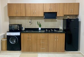 Una cocina compacta con armarios de madera, un microondas integrado, una estufa y un refrigerador negro.