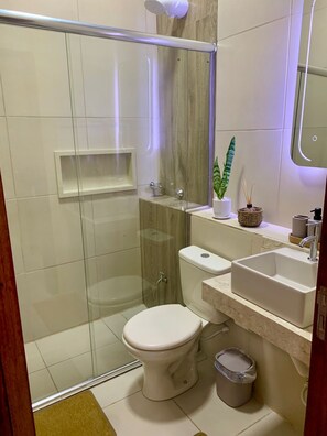 Un baño moderno con ducha envuelta en vidrio, inodoro, lavamanos y una planta pequeña en la encimera.