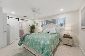 Een slaapkamer met een bed, nachtkastjes, een plafondventilator en een raam met jaloezieën.