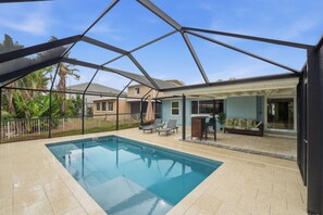 A covered outdoor swimming pool with a patio area, lounge chairs, and a view of neighboring houses. - Waterfront Fort Myers Beach Retreat (Fort Myers Beach)