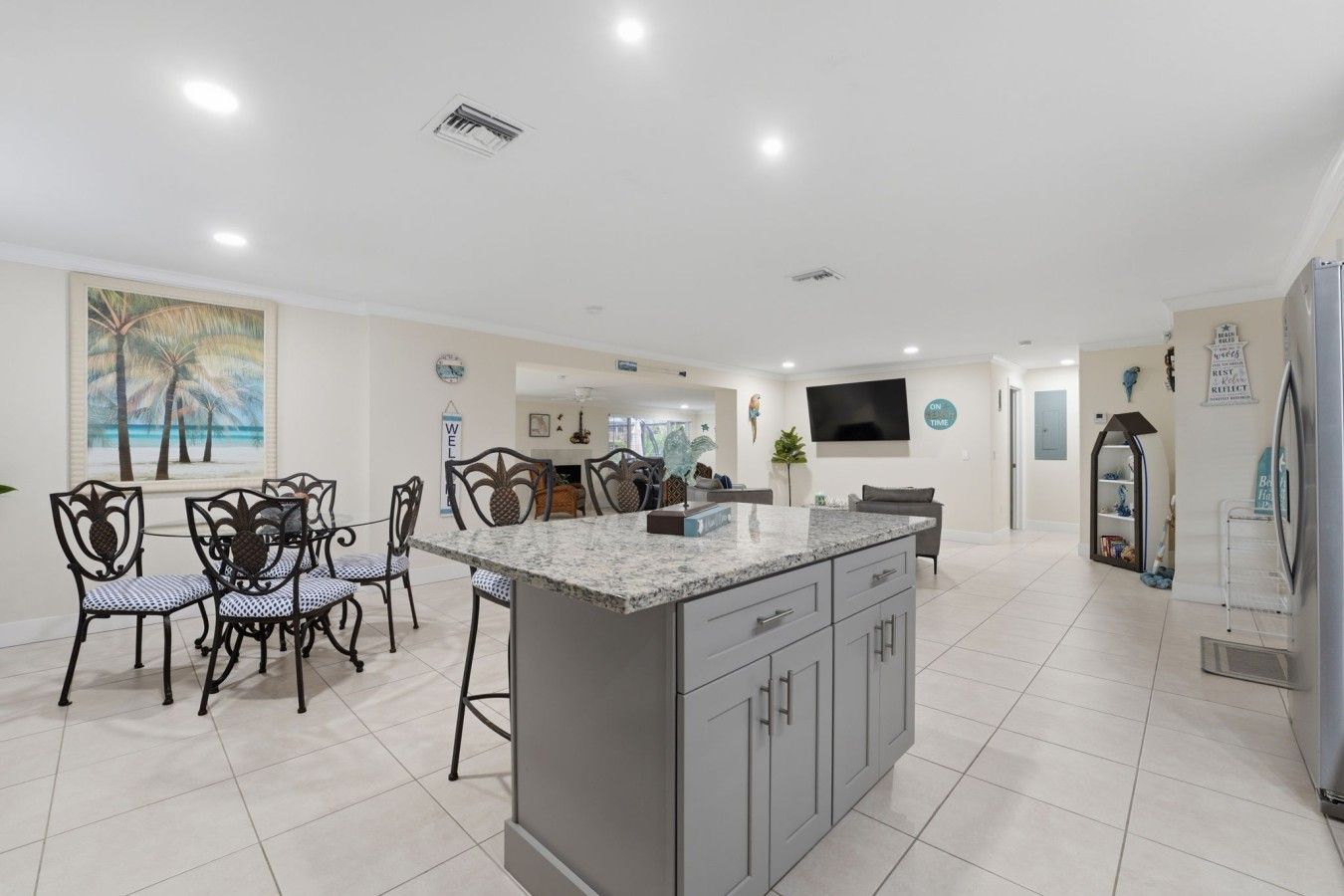 A modern kitchen with a central island, dining chairs, and a TV mounted on the wall.