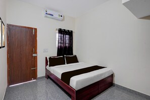 A bedroom with a wooden bed, a window with curtains, a wall-mounted air conditioner, and a door. - Classic White Field CS (Bengaluru)